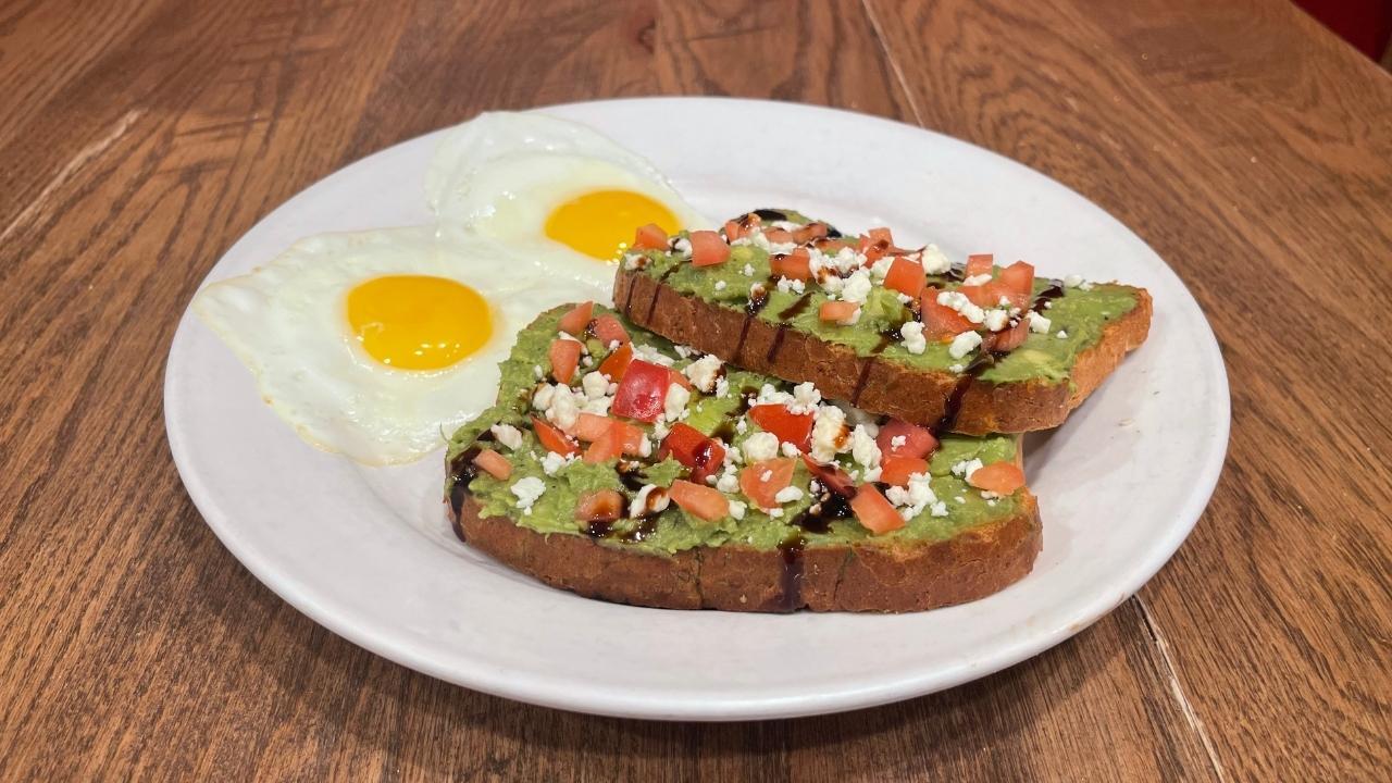 white plate with avocado toast and two eggs.