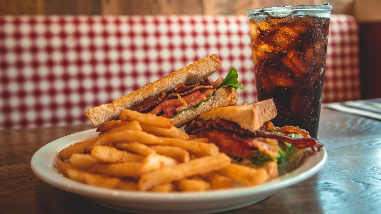 a plate with french fries and bacon, tomato and lettuce sandwich and a cold beverage.